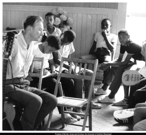Pete Seeger meets with students in a Freedom School class at Mt. Zion Baptist Church in Hattiesburg, Mississippi, on August 4, 1964. Anthony Harris is on Seeger’s left and Herbert Knox is to the right, leaning forward with his elbows on his knees. Photo by Hebert Randall. (c) USM Randall Archives. 
