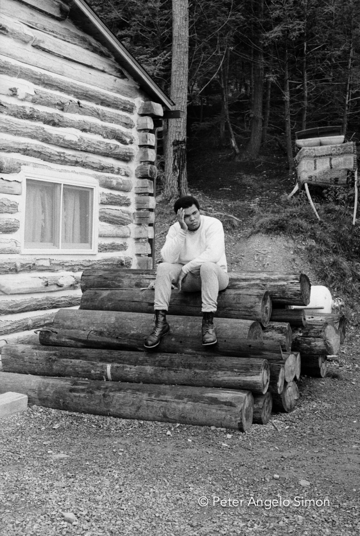 Still without breakfast, Ali rests after the exertion of his dawn run. He called his Deer Lake, Pennsylvania camp “Fighter’s Heaven” and said it was the best camp a fighter ever had.  He had specified that the camp’s buildings be made of logs to give the place the old -time atmosphere he enjoyed. © Peter Angelo Simon, 1974